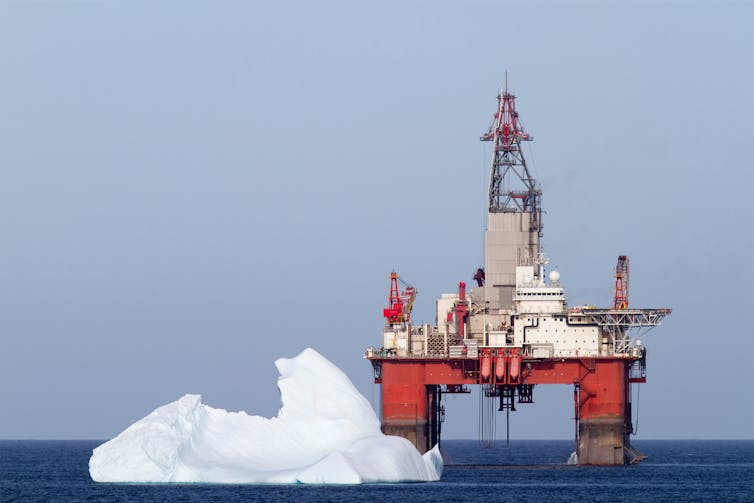 An oil rig with a large iceberg in front of it.