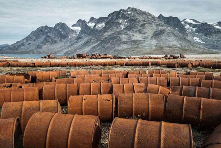 Dozens of rusted drums and mountains in the background.