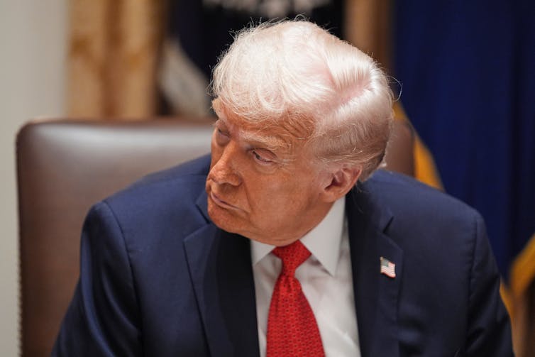 A man with sandy hair dressed in a blue jacket, white shirt and red tie.