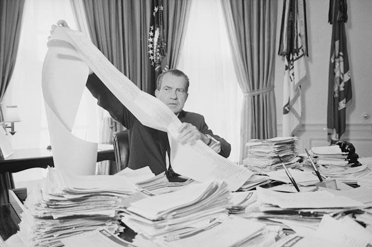 A man holds a long scroll of paper.