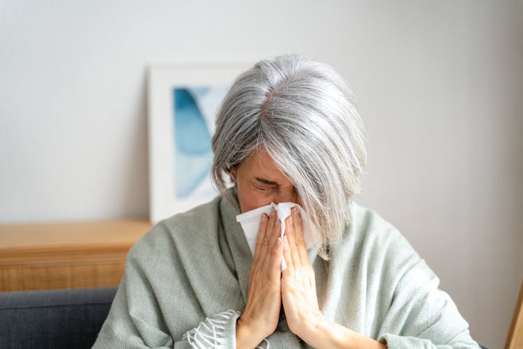 An older woman sneezing into a tissue